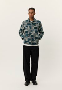 Σχεδιασμένο σακάκι σε μπλε και κρεμ με γεωμετρικά και λουλουδάτα μοτίβα. Διαθέτει τσέπες, κουμπιά και γιακά στο λαιμό. Φοριέται με μαύρο παντελόνι.