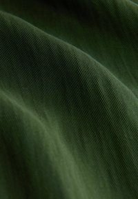 Donkergroene stof met een gladde textuur, voorzien van subtiele ribbels en golven, die de lichte en flexibele eigenschappen van het materiaal benadrukken.