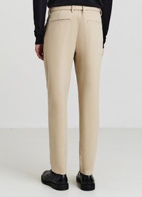 Pantaloni beige realizzati in tessuto liscio, caratterizzati da un design a gamba dritta, con due tasche posteriori e una cintura liscia, abbinati a scarpe nere.
