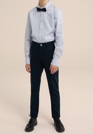 Jasnoniebieska koszula w małe czarne kropki, w zestawieniu z ciemnoniebieskimi spodniami i czarnymi butami. Krawat w czarnym kolorze dodaje formalnego charakteru.