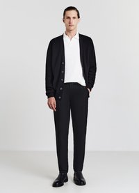 Cardigan nero con bottoni, polo bianca a trama, pantaloni neri e scarpe nere. Design semplice e strutturato.