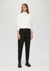 Chemise blanche à boutons avec une poche, associée à un pantalon noir à taille élastique et des bottines noires. Design simple et ajusté avec une texture lisse.