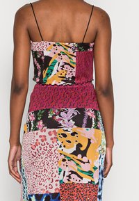 Mönstrad maxiklänning med en lapptäckedesign som inkluderar djurtryck och blommönster. Mjuk textil, justerbara spaghettistövlar och figurnära midja.