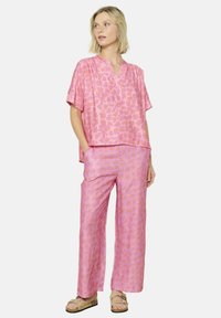 Completo a due pezzi con stampa leopardo rosa, composto da una maglietta a maniche corte con colletto e pantaloni dal taglio largo. Tessuto morbido e leggero.