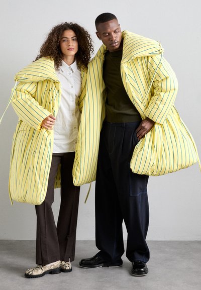 Yellow striped puffer coats with large hoods, paired with dark trousers. Textured snake-print shoes and smooth black footwear complete the look.
