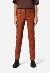 Bruine faux leren broek met een slim fit, voorzien van voorzakken en een ritssluiting. Gladde textuur met een subtiele glans.