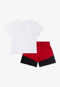 Vit bomullströja och röda shorts med svarta detaljer. Shortsen har ett elastiskt midjeband och en färgblockdesign.