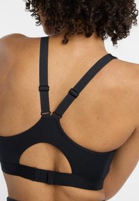 Soutien-gorge de sport noir avec une découpe en trou de serrure à l'arrière, des bretelles réglables et une large bande élastique pour le soutien. Texture lisse.