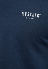 Tumši zila kokvilnas T-krekls ar baltu uzdrukātu logotipu "MUSTANG" un "SINCE 1932." Gluda tekstūra ar apaļu kakla izgriezumu.