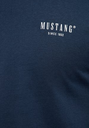 Tamsiai mėlynas medvilninis marškinėlis su baltais spaudiniais, kuriuose parašyta „MUSTANG“ ir „SINCE 1932“. Lygi tekstūra, apvalios kaklo linijos dizainas.