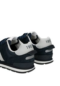 Un paio di sneaker blu navy e bianche con dettagli in suede, pannelli in rete e "1955" stampato sulle linguette del tallone, mostrato dal retro e di lato.