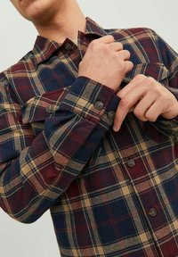 Camisa de franela de cuadros en colores azul marino, burdeos y beige. Tiene mangas largas, cuello y puños abotonados con una textura suave.