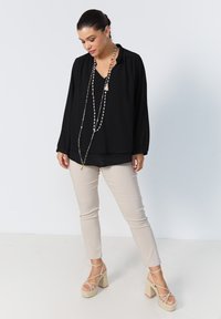 Black long-sleeve blouse with a V-neck, paired with beige fitted pants and strappy wedge sandals. A layered beaded necklace completes the look.
