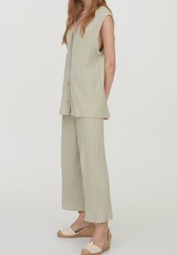 Conjunto de tela acanalada de color verde claro que consta de una blusa sin mangas con escote en V y botones, junto con pantalones de pierna ancha, combinados con sandalias de cuña beige.