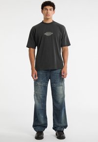 Donkergrijze T-shirt met korte mouwen en het logo "ORIGINALS", gecombineerd met wijde blauwe denim cargobroek met meerdere zakken en versleten details.