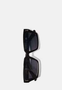 Mustat ylisuuret aurinkolasit, joissa on paksu kehys, tummat linssit ja kultaiset yksityiskohdat sangoissa. Sileä muovimateriaali.