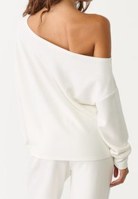 Pull blanc à épaules dénudées, coupe ample, manches longues et texture douce. Design simple, avec un ourlet décontracté.