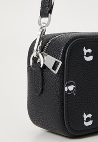 Black textured leather crossbody bag with silver hardware, featuring a zipper closure and playful graphic accents on the front.