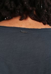 Tissu léger gris foncé avec une texture lisse et un col en scoop. Comprend une petite étiquette "Key Largo" près de la couture arrière.