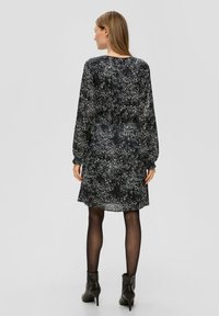 Schwarzes Kleid mit weißen Sprenkeln, langen Ärmeln, tailliert und mit einem fließenden Rock. Getragen mit schwarzen Stiefeletten und transparenten Strumpfhosen.