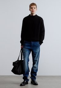 Mustast soonikuga kampsun, sinised teksad tuhmendatud viimistlusega, mustad nahast kingad ja must ostukott. Lihtne, modernne disain.