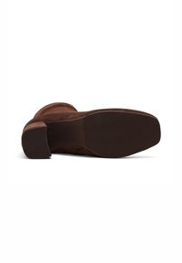 Bottine en daim marron allongée sur le côté, montrant un bout carré et un petit talon carré avec une semelle texturée.