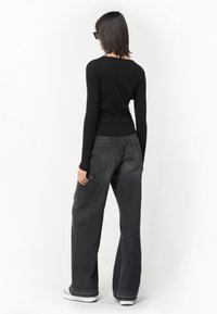 Haut noir à manches longues côtelé associé à un pantalon en denim gris ample avec deux poches arrière et une coupe décontractée. Des chaussures noires complètent la tenue.