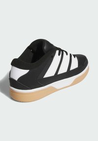 Svartvit sneaker med gummisula, som har tre svarta ränder på sidan och en strukturerad svart ovandel.