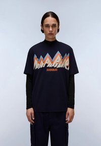 Tamsiai mėlynas marškinėlis su kalnų grafika oranžiniais, mėlynais ir baltais atspalviais, su tekstu „NAPAPIJRI“ ryškiu, stilingu šriftu.