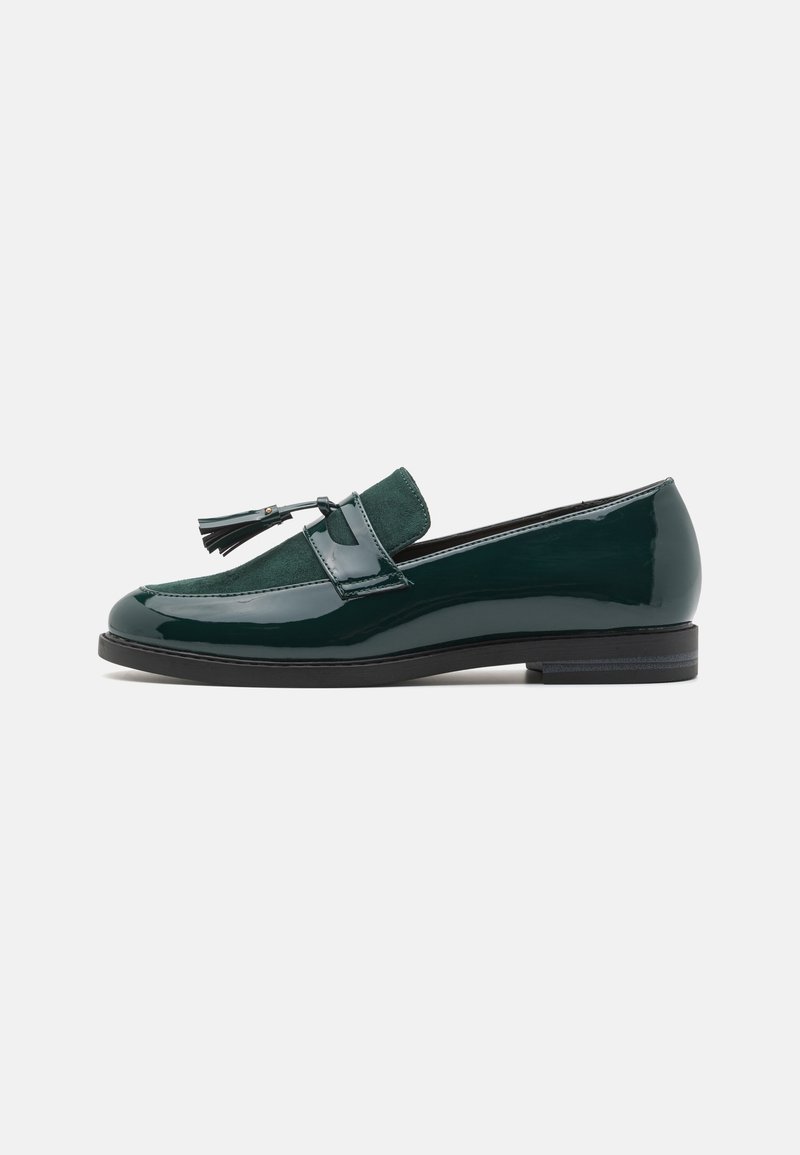 Mocassins vert foncé avec une finition brillante en cuir verni, des accents en daim et des pompons décoratifs à l'avant. Semelle plate noire, design à bout arrondi.