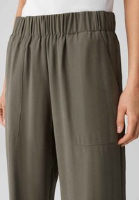 Pantalons à taille élastique en vert olive, avec une texture lisse, des jambes larges et des poches latérales pour une fonctionnalité accrue.