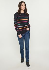 Pulover negru cu dungi orizontale multicolore. Textură tricotată, manșete și tiv ondulate. Potrivit cu blugi albaștri și adidași negri.