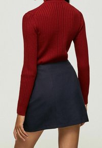 Un pull à côtes rouge avec des manches longues associé à une jupe bleu foncé. Le pull présente un col montant et une silhouette ajustée.