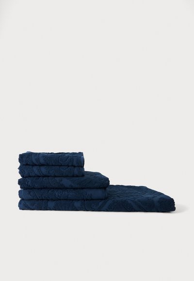 Pile de cinq serviettes bleu foncé pliées avec des motifs floraux texturés sur un fond clair uni.