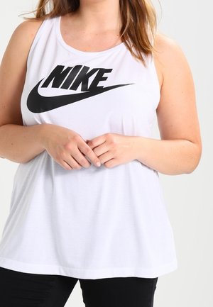 Kobieta nosząca biały, bezrękawnikowy top Nike z czarnym logo, z rękami splecionymi przed sobą, na jednolitym jasnym tle.
