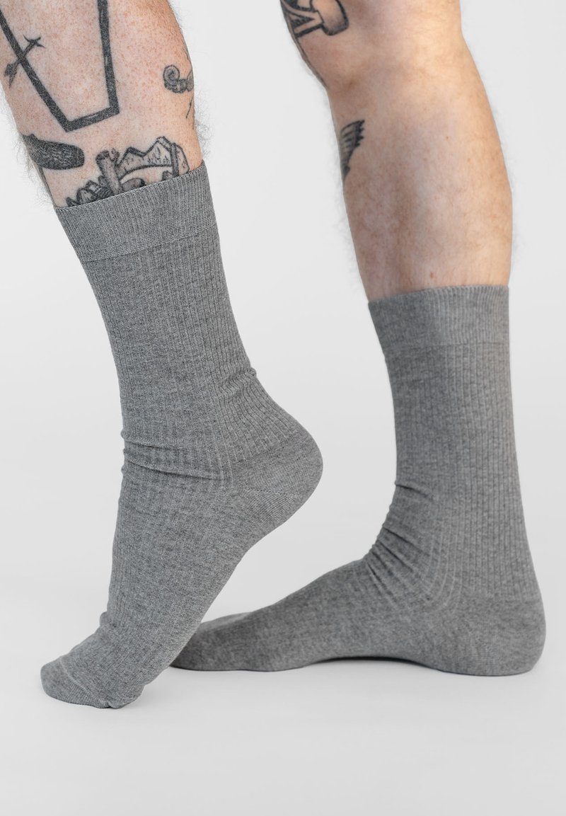 Graue, gerippte Socken in mittlerer Wadenlänge mit einer weichen Textur und elastischen Bündchen für einen guten Sitz. Die Details umfassen ein glattes, einheitliches Muster.