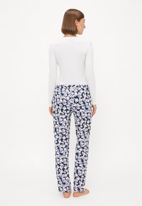 Haut blanc à manches longues associé à un pantalon imprimé floral marine comportant des fleurs roses et bleues sur un tissu texturé.