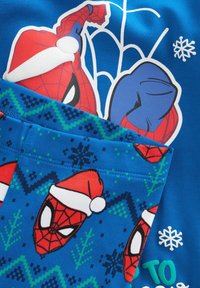 Spider-Man che indossa un cappello di Natale su un tessuto blu con fiocchi di neve e motivi a maglia a tema festivo in verde e blu navy.