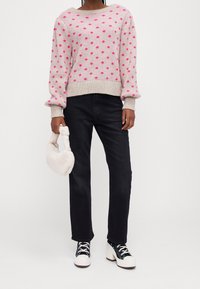 Suéter gris claro con lunares rosados, escote redondo y puños acanalados, combinado con jeans negros de pierna recta y zapatos de plataforma blancos.
