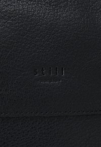 Zwarte leren accessoire met een gestructureerd oppervlak, met het reliëfmerk "still" en "nordic." Eenvoudig ontwerp met nette stiksels.