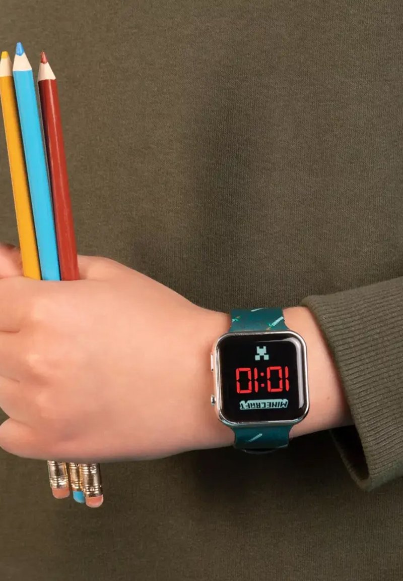 Digital watch with a rectangular black face displaying red numbers. Teal silicone band features a pattern of small graphics.