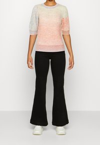 Maglione a maglia multicolore con maniche corte a sbuffo, caratterizzato da un motivo testurizzato; abbinato a pantaloni neri a gamba larga e sneakers bianche.