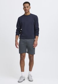 Navy Sweatshirt mit Rundhalsausschnitt, kombiniert mit grauen Shorts. Die Materialien wirken weich, mit gerippten Bündchen. Die Schuhe sind hellgrau mit Schnürsenkeln.