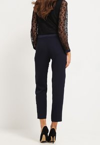 Námořnické kalhoty s úzkým střihem a hladkým předním dílem. Mají hladkou texturu a zkrácenou délku. Kombinovány s černým krajkovým topem s dlouhými rukávy.