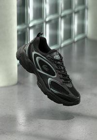 Μαύρο αθλητικό παπούτσι με πλέγμα και συνθετικό υλικό, με υφή στην σόλα, κομψό σχέδιο, ασημί λεπτομέρειες και μπροστινό δέσιμο με κορδόνια.