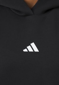 Sweatshirt preto com um logótipo branco de três riscas na frente. O tecido parece macio, com uma textura suave e um corte descontraído.