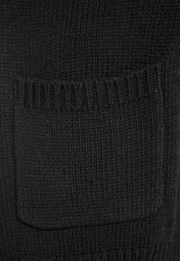 Czarna dzianina z wyraźną kwadratową kieszenią z prążkowanym wykończeniem u góry, prezentująca miękki i teksturowany wygląd.