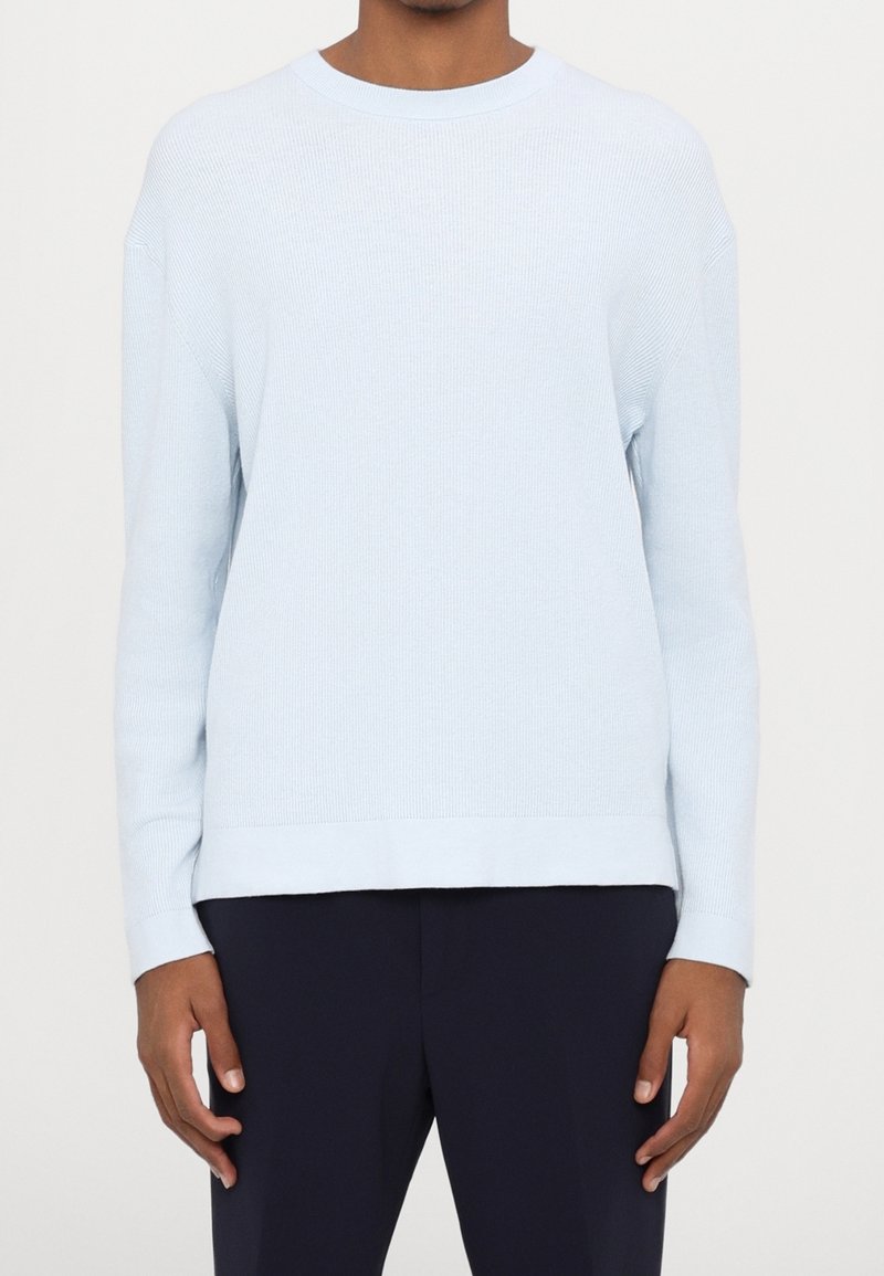 Jasnoniebieski sweter z długim rękawem o prążkowanej fakturze i okrągłym dekolcie, charakteryzujący się luźnym krojem i prostym dołem. Noszony na ciemnych spodniach.