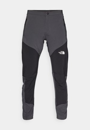 Sorte og grå utendørbukser med en tettsittende design, som har glidelåslommer og en logo på fronten. Laget av lett, slitesterk materiale.