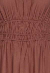 Tissu marron avec couture élastique froncée créant une texture froncée et des bandes horizontales sur toute la surface.